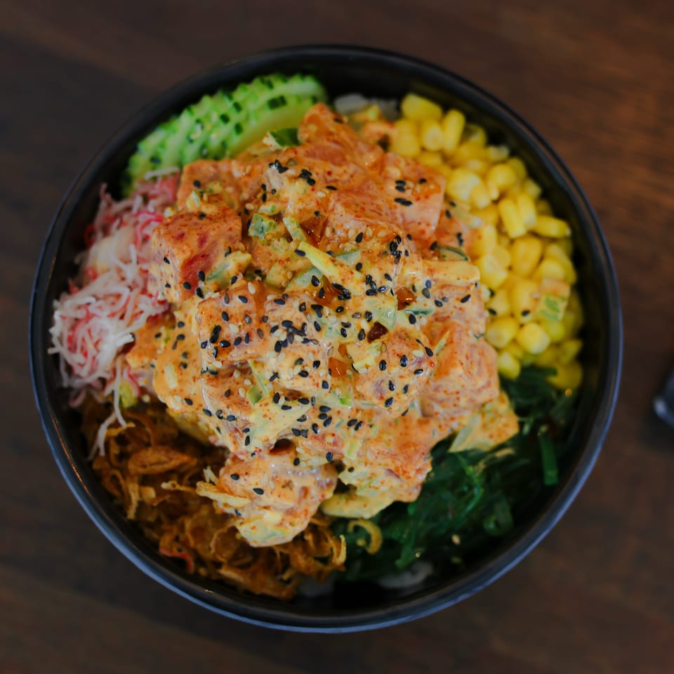 Spicy salmon poke bowl with creamy aioli, crab, corn, avocado, seaweed, and crispy onions.
