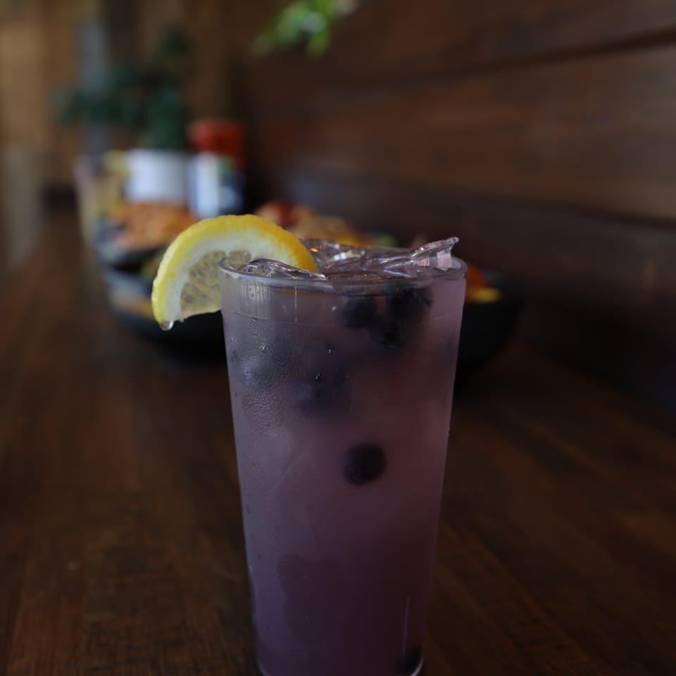 Blueberry lemonade over ice with fresh blueberries and a lemon slice.
