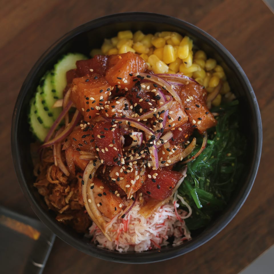 Tuna and salmon poke bowl with red onion, crab, corn, cucumber, seaweed, and crispy onions.